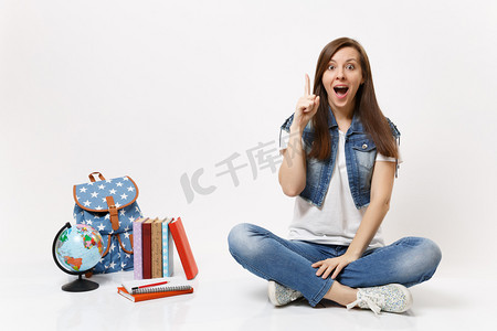 年轻兴奋的女学生用新思想启蒙, 点子指向食指上坐近地球仪, 背包学校的书被隔离在白色的背景上。高中院校教育