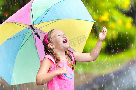 奔跑的孩子摄影照片_孩子在雨中玩耍。孩子们带着雨伞在外面下大雨.第一次春雨中被抓住的小女孩。秋天的雨天使孩子们在户外玩得很开心.在热带风暴中奔跑的儿童.