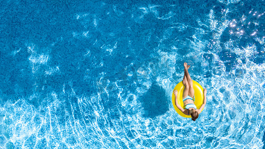 活跃的少女在游泳池空中俯瞰，孩子们在充气的环形甜甜圈上放松和游泳，在家庭度假、热带度假胜地玩水玩乐