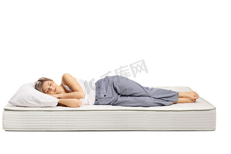 穿着睡衣的年轻女子睡在舒适的床垫上，床与白色背景隔离