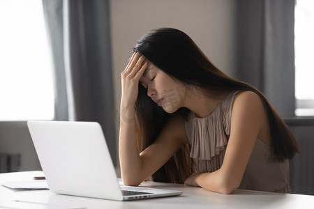 烦躁女摄影照片_长期使用笔记本电脑后头痛的疲惫的亚洲女商人