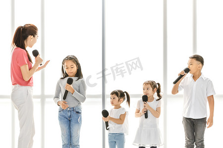 亚洲老师教亚洲孩子唱歌, 孩子们注意听她说话, 他们站在白色的大窗户前。音乐学校或歌唱课堂训练的概念.