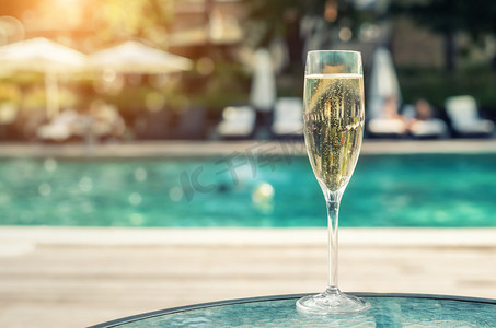 蓝色饮料摄影照片_在度假期间，豪华度假酒店在泳池边提供白色香槟或散装玻璃。带上升气泡的起泡酒，室外有蓝色泳池背景。清凉酒精饮品
