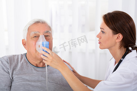 年轻的女医生持有氧气面罩在高级男性患者的脸上