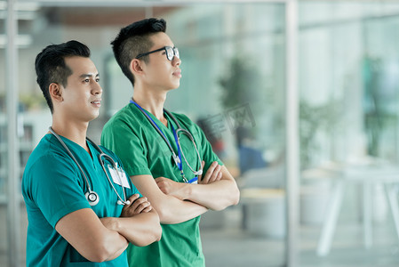 两名亚洲卫生专业人员站在医院大厅模糊的背景上, 双手合十, 望着自己