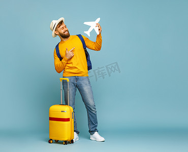 黄色页摄影照片_全身上下喜怒无常的男人笑着指着玩具飞机，站在蓝色背景的行李旁边