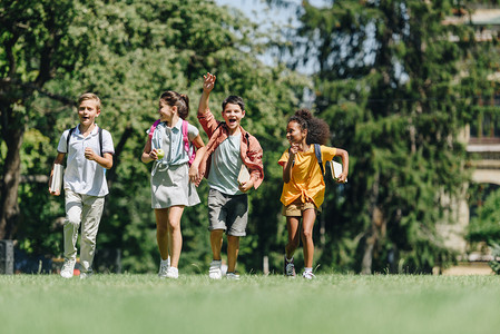 四个快乐的多元文化学童在公园的绿色草坪上奔跑 