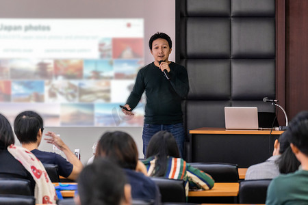 亚洲演讲者或演讲人在舞台上通过投影仪屏幕在会议厅或研讨会会议室向观众演示，商务教育和研讨会概念