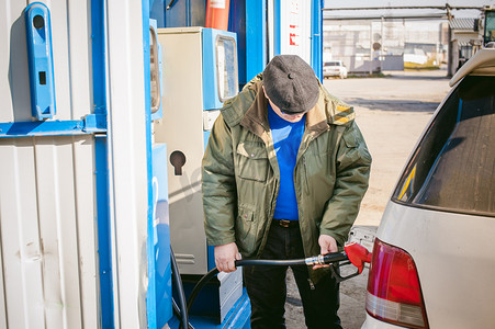 男子在一个加油站填充车辆油箱燃料。成年男子与一个小胡子和眼镜，加油前长途旅行的道路上向非网络加油站汽车