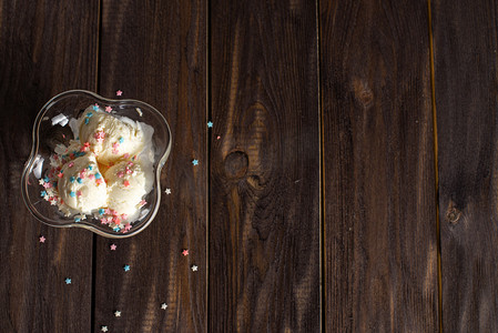 白色的香草冰淇淋球，在色彩艳丽的洒水下，放在一个甜点碗里。深色木桌上装饰过的冰淇淋.