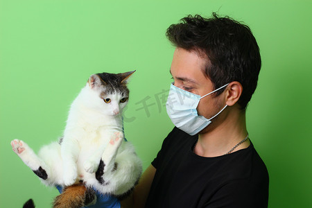 那只猫在一个戴外科医疗面具的男人手里。绿色背景爱护动物的概念