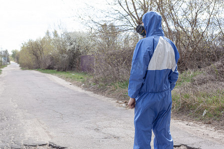 蓝色背摄影照片_身穿蓝色防护工作服，戴着呼吸面具的男子背对着背站在路上。检疫大流行病covid-19
