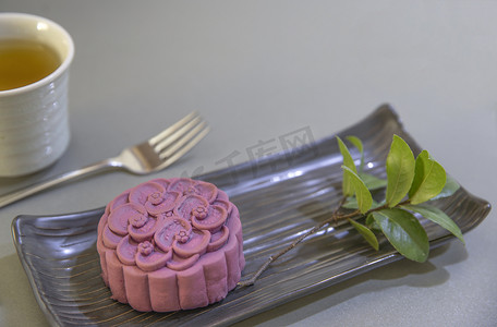 月饼背景摄影照片_一种非传统的中国月饼，用紫色的日本山药和一杯绿色的黑色陶瓷盘做成。顶部视图，灰色计数器顶部背景.