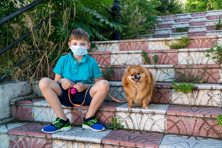 Coronavirus covid-19概念。一个戴着医疗面具的小男孩带着狗散步。在户外戴口罩的儿童。新的现实.