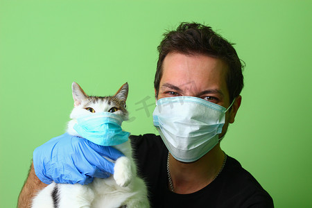 爱护动物摄影照片_头戴医用外科口罩的年轻人或男人和猫。Covid-19大流行病期间爱护动物的概念