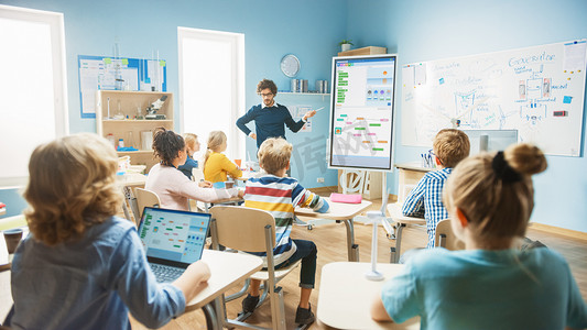 小学计算机科学教师使用交互式数字白板向充满聪明多样化儿童的课堂展示编程逻辑。有孩子在听的电脑课