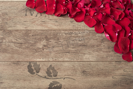 红色的玫瑰花瓣洒在木制的背景。玫瑰花瓣边框，木制的桌子上。顶视图，复制空间。花卉的框架。市场营销摄影的风格。婚礼、 礼品卡、 情人节或母亲节 bac