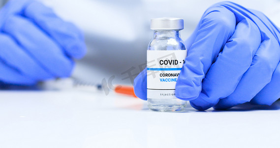 疫苗瓶摄影照片_科罗纳病毒疫苗的概念，医生手戴蓝色医用手套与透明液体科罗那韦疫苗瓶和注射器在实验室注射。新的疾病治疗方法的研究与开发