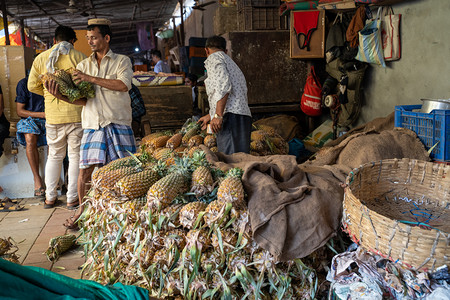 work摄影照片_Mumbai, India - February 29, 2020: Vendors selling pineapple fruit hard at work in the Crawford Market, known for its fresh fruits and vegetables
