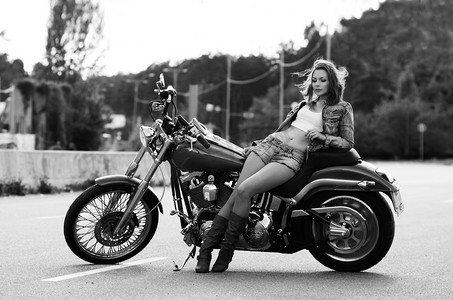 漂亮苗条的年轻女人 （女孩） 站，靠在一辆摩托车，背景下的城市景观。模糊的背景。在日光下拍摄。全长画像。休闲和旅行在摩托车上的概念. 