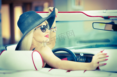 户外夏天的驾驶一辆敞篷车的红色复古时尚复古美女的画像。时尚迷人金发女性，红色汽车的黑帽子。阳光明亮的颜色，在户外拍摄.
