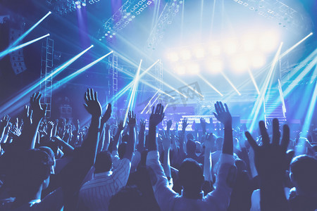 年轻人与愉快的晚上在音乐会, 人群用举起的手站立在蓝色光, 唱歌和享受音乐概念