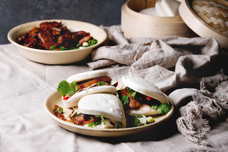 亚洲三明治, 配有猪肉肚, 青菜和蔬菜, 配有亚麻桌布的陶瓷盘子。亚洲式快餐晚餐.