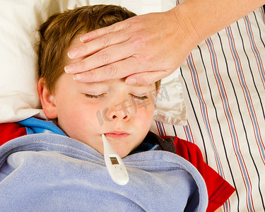 发烧温度摄影照片_生病的孩子男孩正在发烧和病在床上休息的同时检查