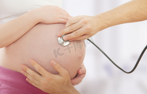 孕妇和手的医生用听诊器的肚子里