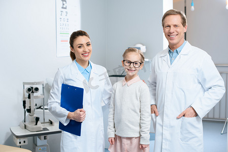 两个微笑的眼科医生和小孩子在眼镜站在诊所