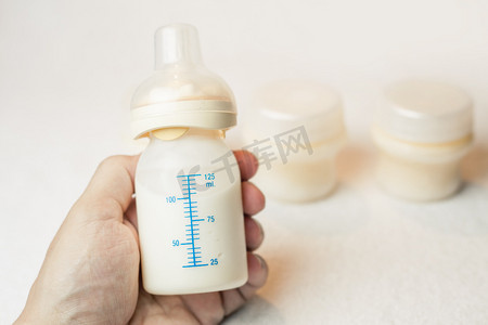 儿童baby摄影照片_Father holding a baby bottle with breast milk with scale
