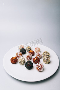 芝麻球摄影照片_干果和芝麻籽的甜食美味的能量球与干果和坚果在椰子片上的白盘子