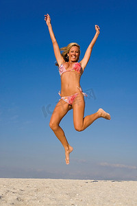 一个美丽的年轻金发女子跳高的沙滩上