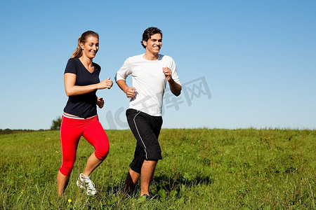 户外做运动摄影照片_年轻的健身夫妇在户外做运动，在晴朗的蓝天下，在青草丛中的夏季草地上慢跑