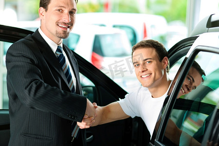 一个人坐在他的新车里在经销商那里买了一辆车；他们正在握手以达成交易