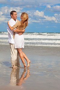 玩沙子摄影照片_一对年轻的男女在海滩上作为浪漫的情侣玩得很开心