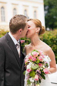 婚嫁摄影照片_新郎在公园亲吻新娘，她手里拿着一束鲜花