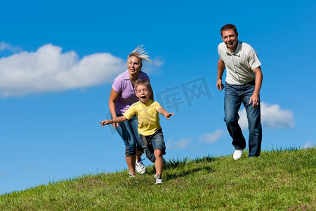 在一个美丽的夏日，快乐的一家人在户外的一条土路上奔跑--他们试图抓住对方
