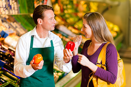 一名妇女在超市的菜架上买杂货，一名店员正在帮助她