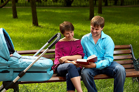 一对夫妇带着孩子散步，坐在公园的长凳上，以草坪为背景阅读这本书