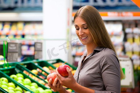 一名妇女在超市货架上买水果，她正在查看苹果。
