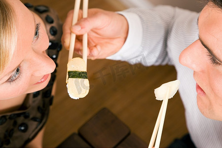 情侣们用寿司互相喂对方吃晚餐，浪漫的场景，想必这是一次提前的约会;浅聚焦在眼睛上