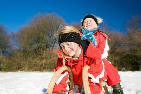 两个小孩子在雪地里的山顶上拉着雪橇，等着开始玩
