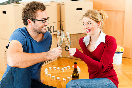 搬进房子或公寓的年轻夫妇，他们坐在木地板上，喝着香槟，在装修中休息。