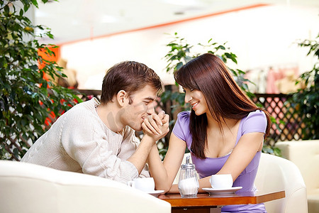 年轻男子在咖啡馆里向美丽的女孩吻手