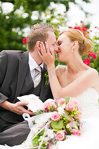 婚嫁摄影照片_新郎在公园亲吻新娘，他拿着戒指，背景是玫瑰花