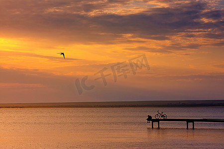 孤寂摄影照片_夕阳西下，一个小渔夫骑着自行车停在码头上。