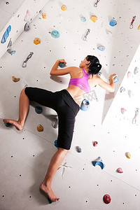 一名女子在健身房的攀岩墙上锻炼手臂和上半身。