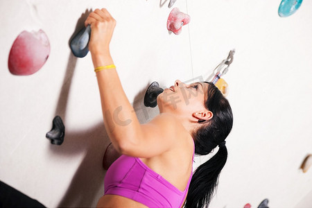 上半身摄影照片_一名女子在健身房的攀岩墙上锻炼手臂和上半身。
