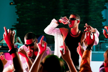 歌手摄影照片_说唱或嘻哈音乐家在俱乐部的舞台上，在欢呼的人群面前表演